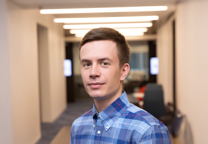 A color photo of a man smiling for a photo in a hallway.