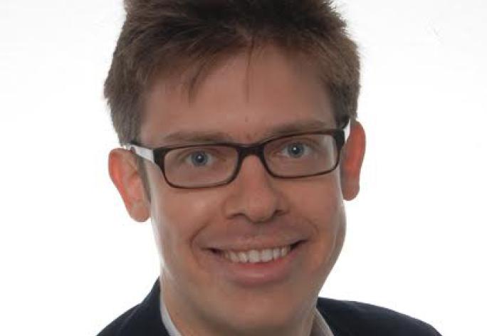 A photo of Immanuel Trummer, a man with short brown hair, glasses,and a white shirt with a black jacket in front of a white background