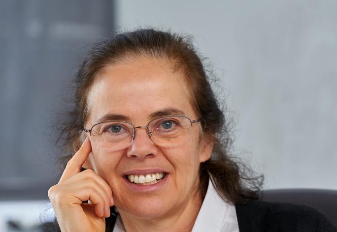 A photo of Éva Tardos, a woman with long brown hair, glasses, a white shirt and black cardigan