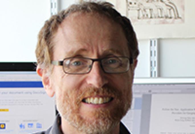 The head and shoulders of a man with glasses, reddish hair and beard, and a striped shirt.