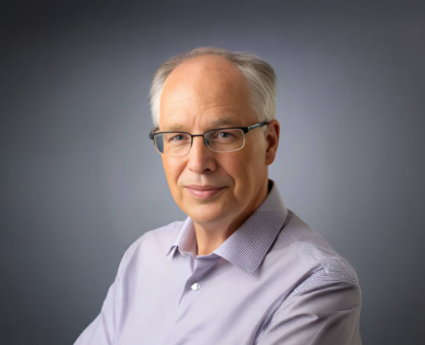 A photo of Bart Selman, a man with white hair and glasses in a lavender shirt in front of a gray background