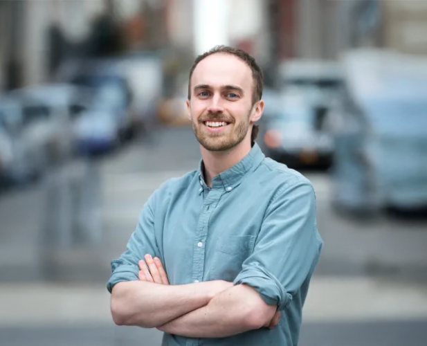 A color photo of a man standing with his arms crossed.