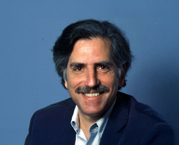 A color photo of a man smiling for a portrait.