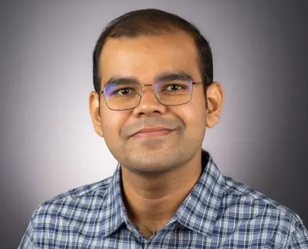 A man with short dark hair, glasses and a blue plaid shirt