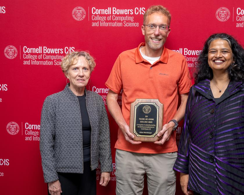 Three people stand in front of a red Cornell step and repeat.