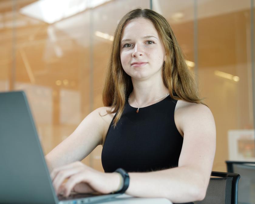 a female student with light brown hair sits in front of a laptop
