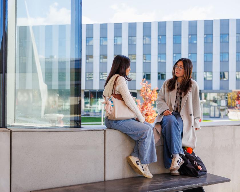 two students sit on ledge outside Gates Hall