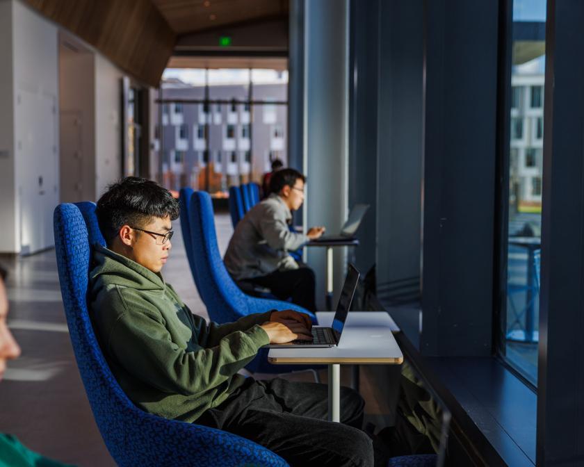 three students sit in blue chairs in front of windows in the new Bowers building