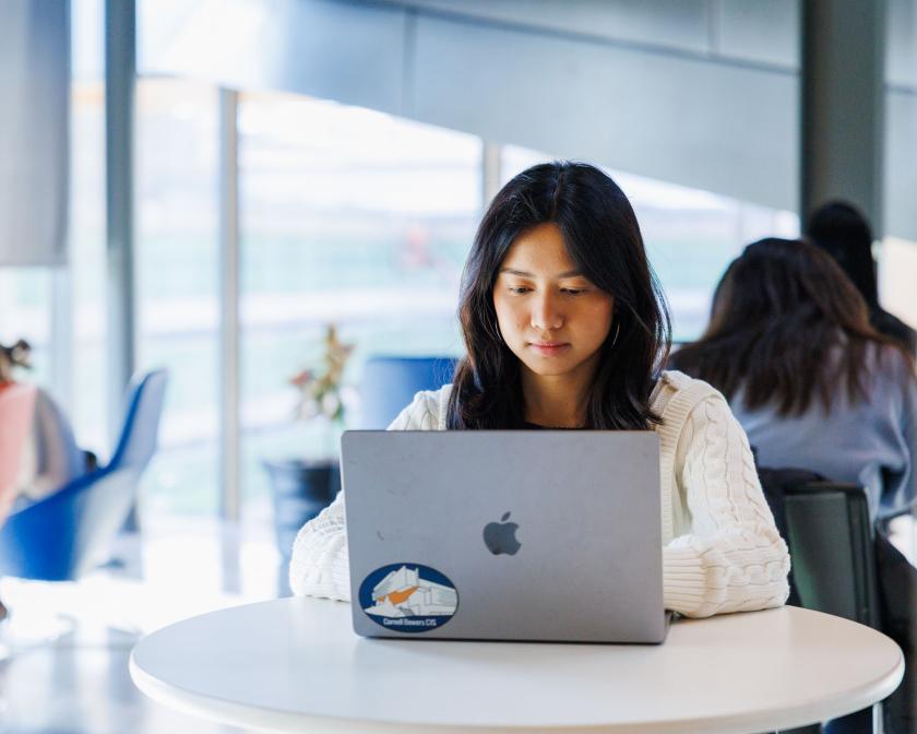 a young female students works on her laptop sitting at a table