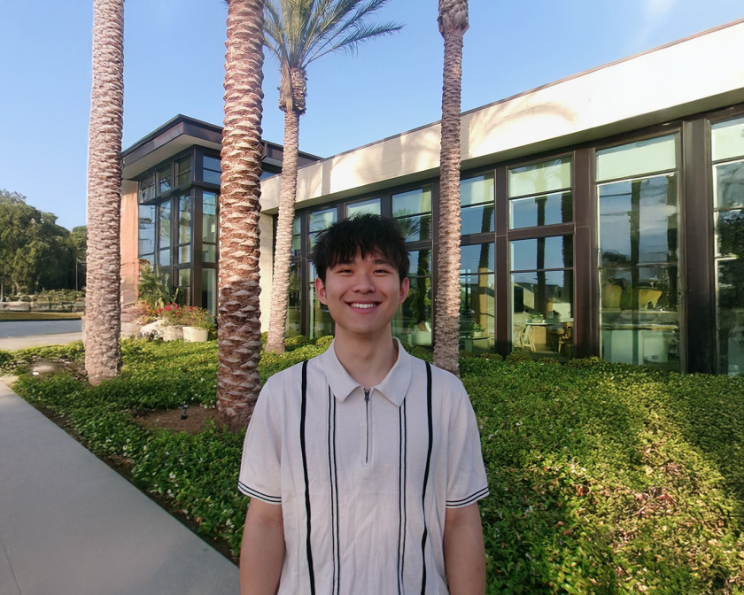 A color photo of a man smiling for a photo outside.