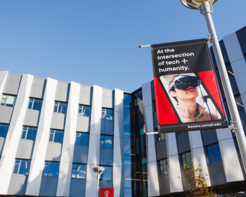 The facade of the Computing and Information Science Building and a lamppost flag that says "At the intersection of tech + humanity"