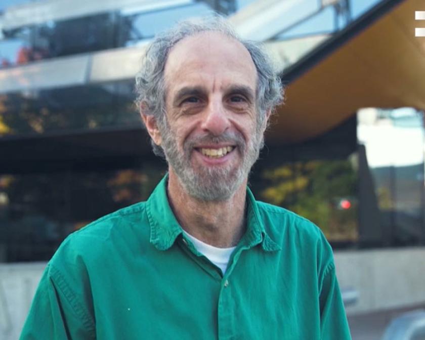 man in green shirt smiling in front of Gates Hall