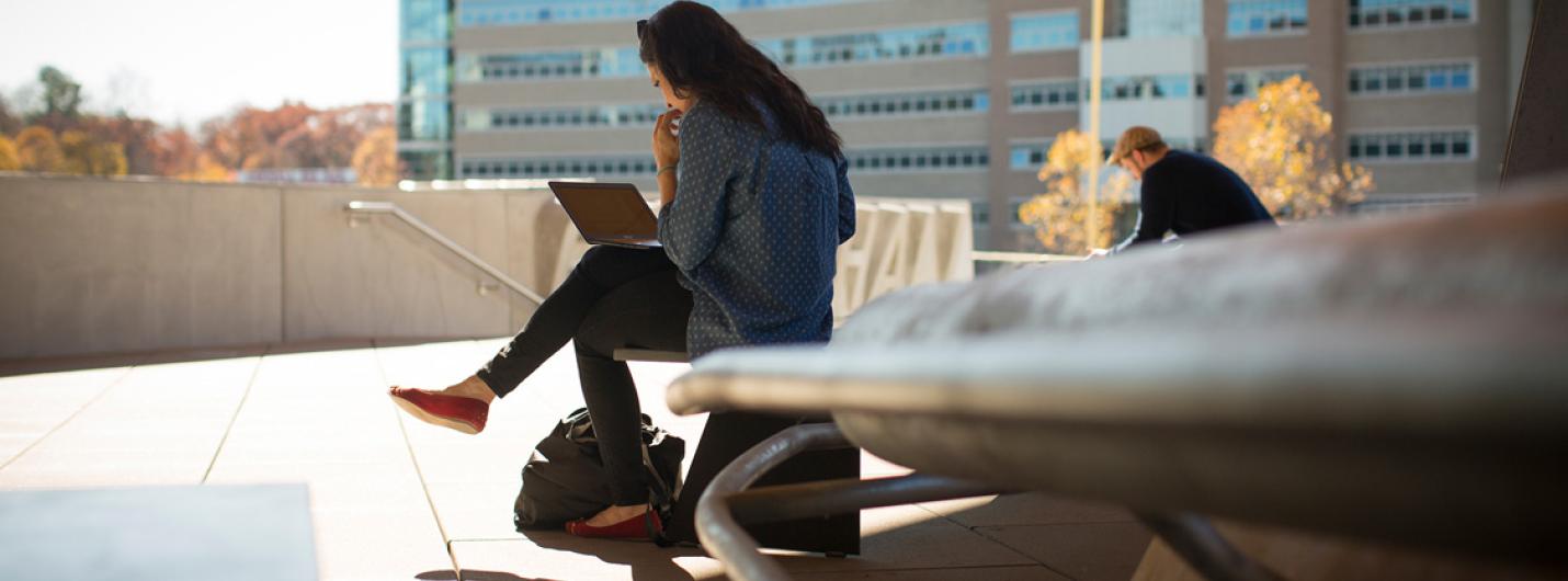 a female student with long brown hair sits on a chair outside gates hall