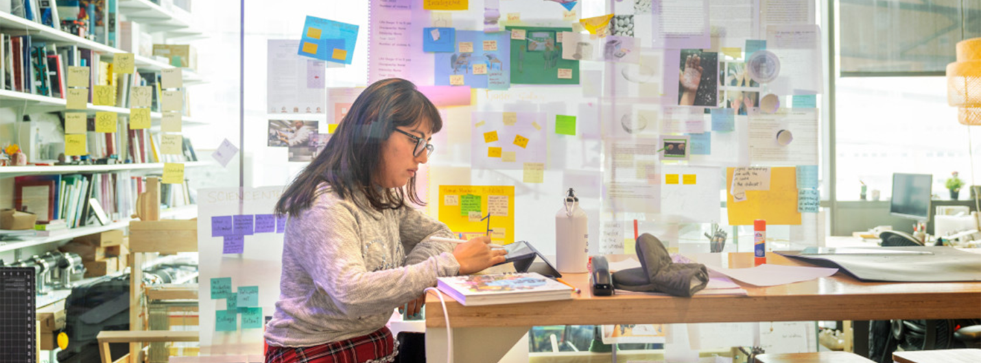 Student works at a desk surrounded by colorful sticky notes and research materials.