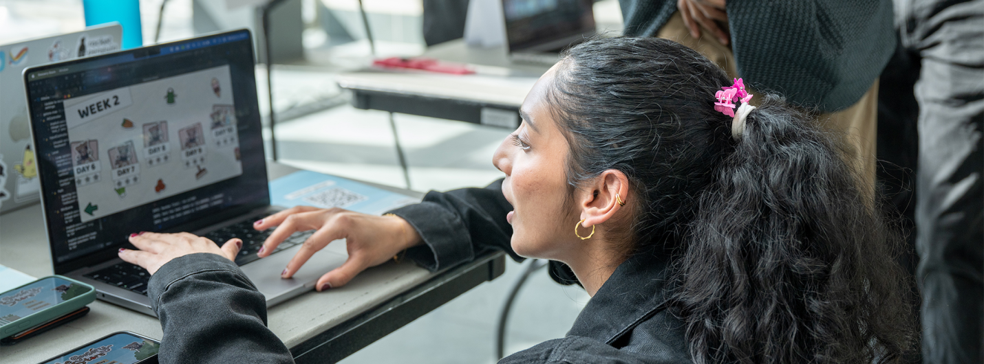 Student demonstrates a project on a laptop at a showcase event.