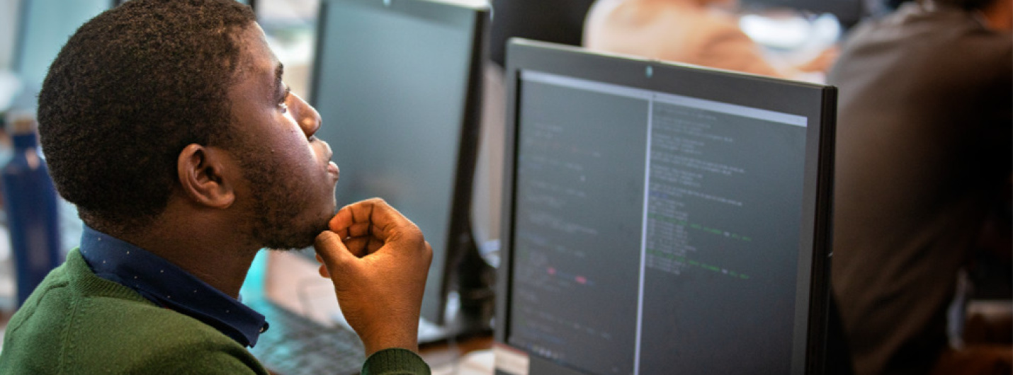 A student looks at code on a desktop computer screen in a classroom.
