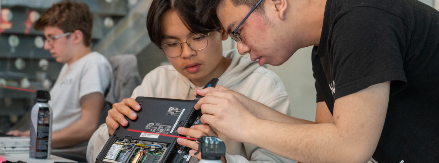 A color photo showing 2 people working to repair a computer.