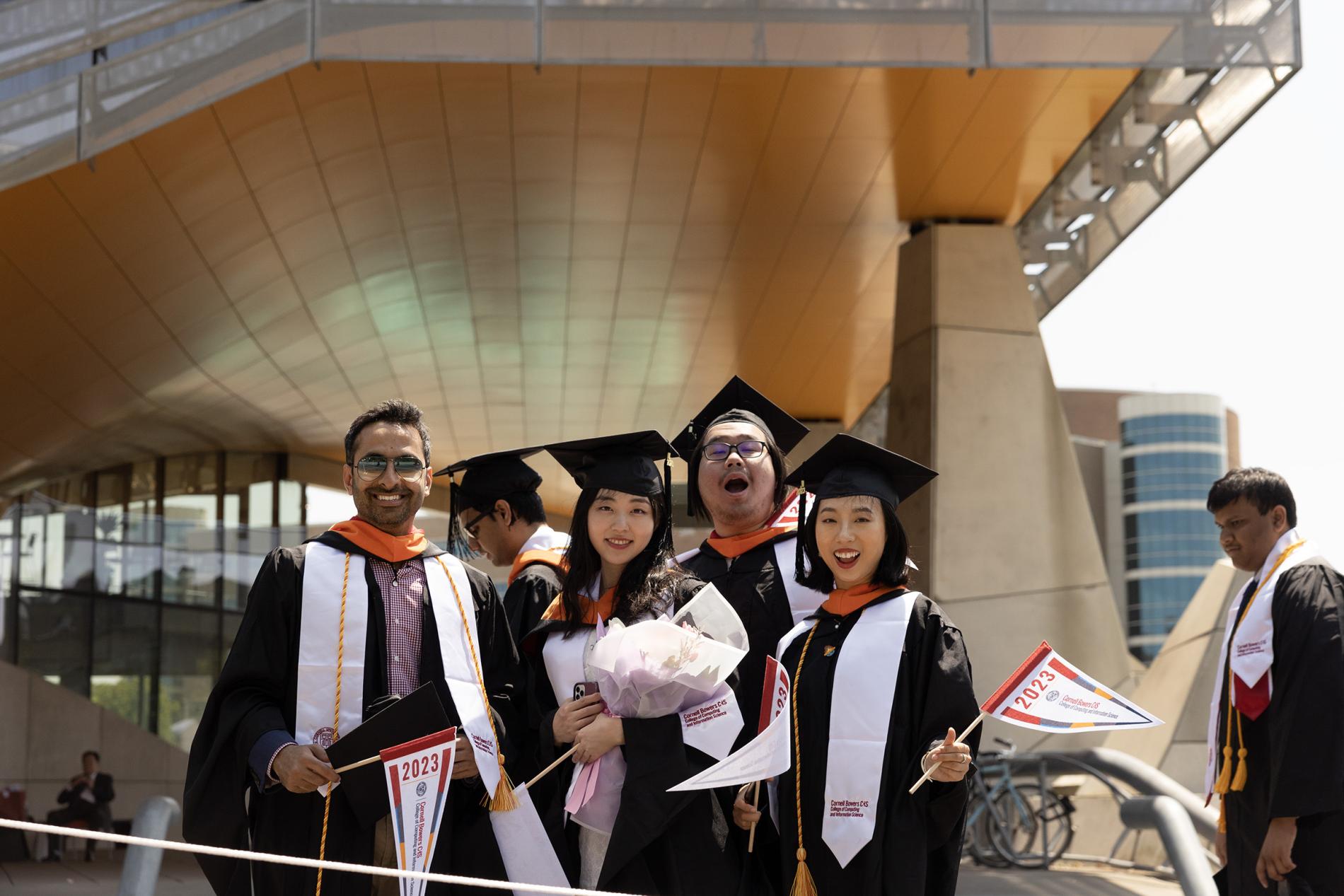 a group of students wave flags and smile outside the orange overhang of Gates Hall