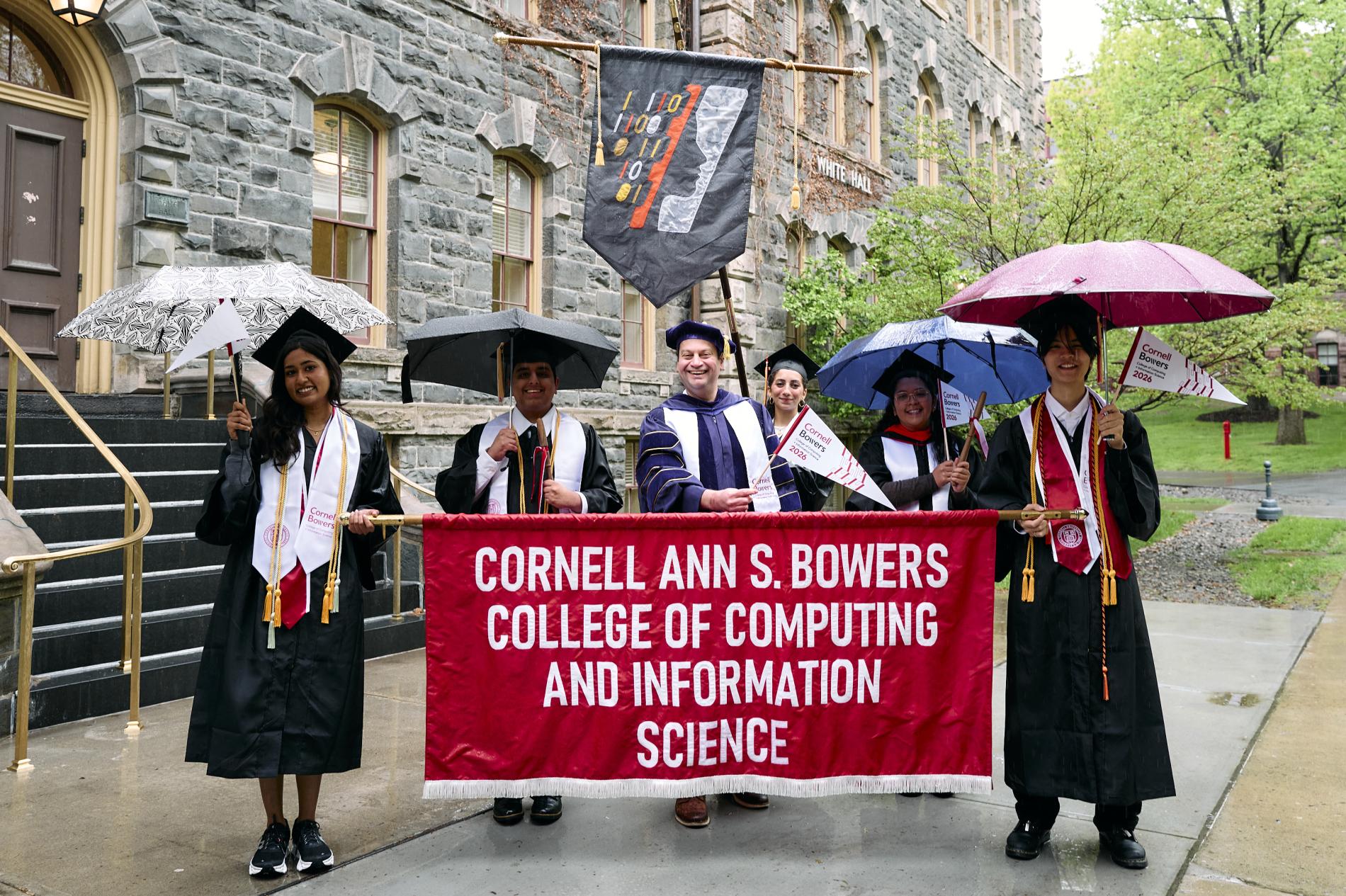 graduates stand behind the red bowers commencement banner