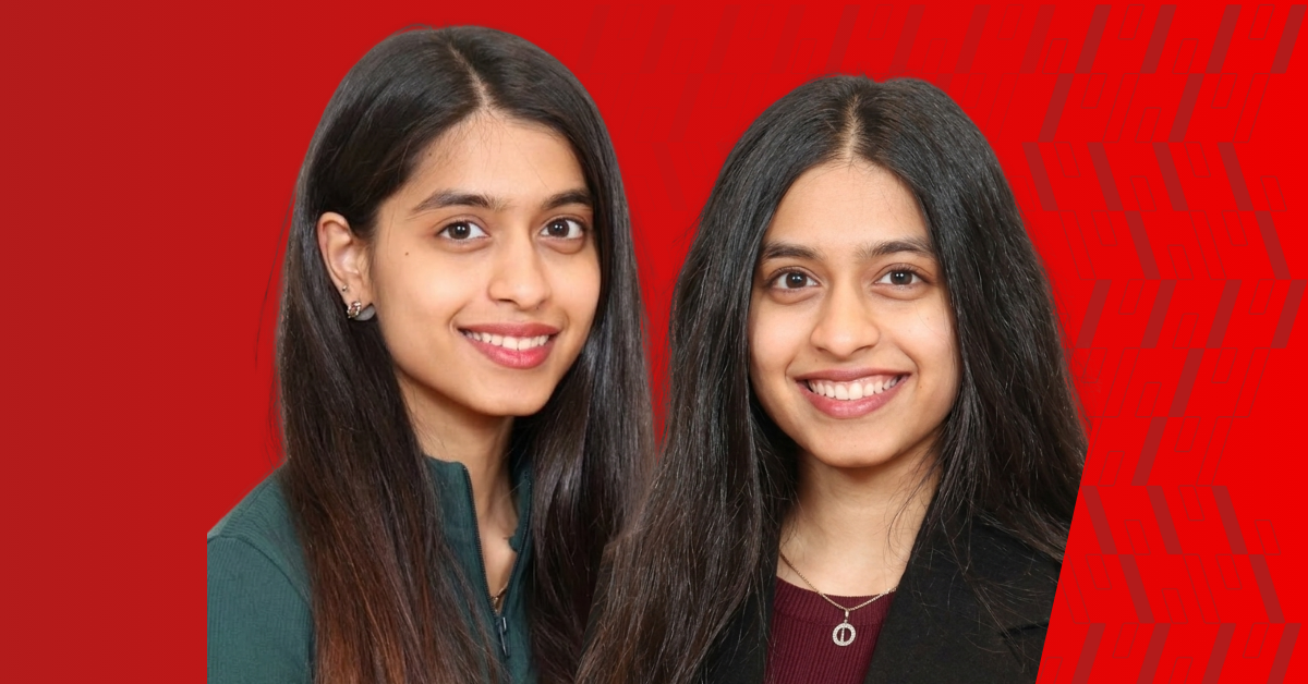 two female students with long dark hair smile against a bright red background